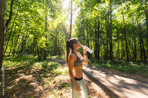 Young woman drinking water after running outdoors