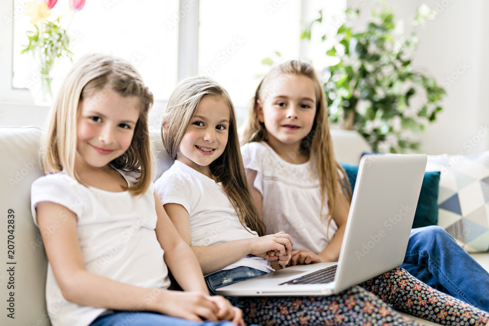 Happy little girls at home working with a laptop on sofa Happy little girls at home working with a laptop on sofa