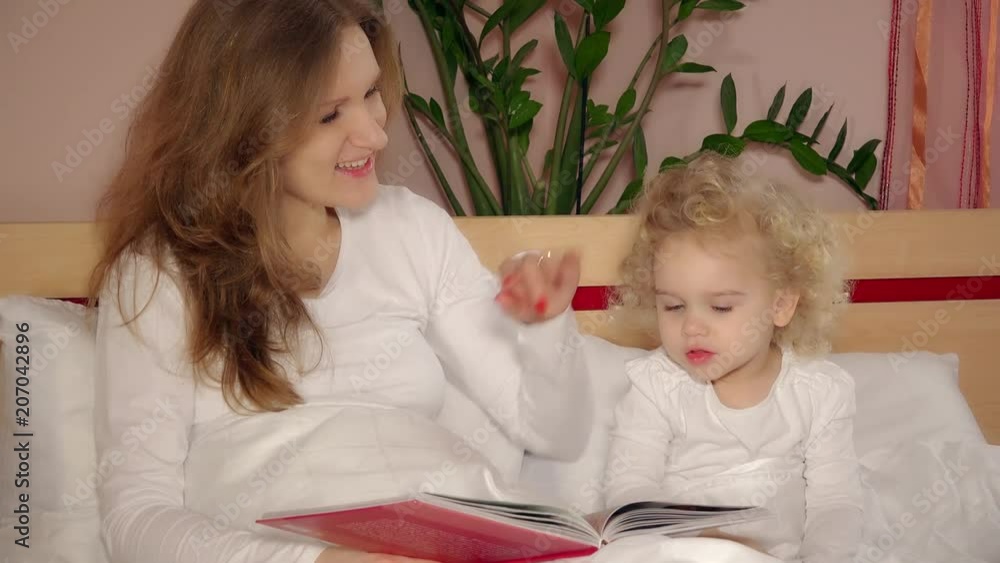 Happy embraced mother and cute daughter girl reading book before sleep