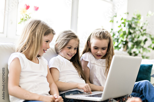 Happy little girls at home working with a laptop on sofa