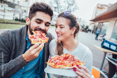 Couple eating pizza outdoors and smiling.They are sharing pizza in a outdoor cafe.