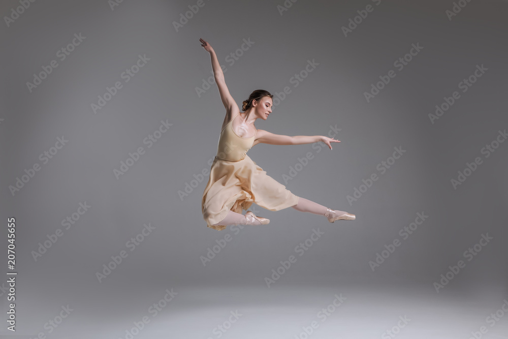 Obraz premium Show yourself! Beautiful good-looking gorgeous ballerina showing classic ballet poses and jumping into the air on the grey background.