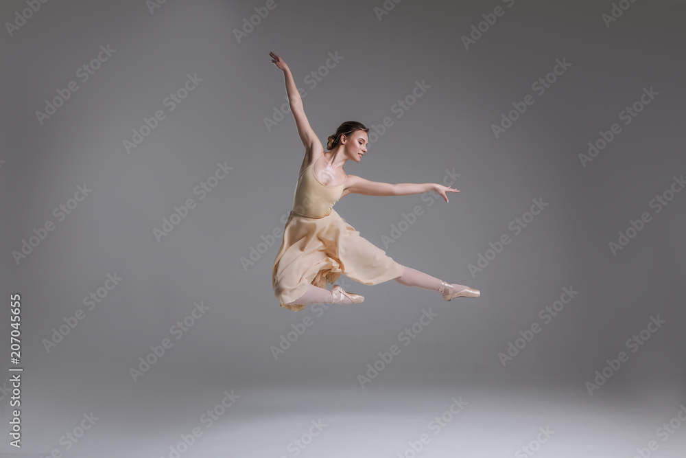 Show yourself! Beautiful good-looking gorgeous ballerina showing classic ballet poses and jumping into the air on the grey background.