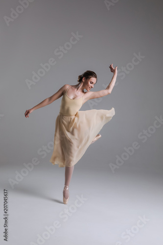The tune of dancing feet! Full length photo of the young attractive enthusiastic ballerina dancing, while rising her leg on the beige background.