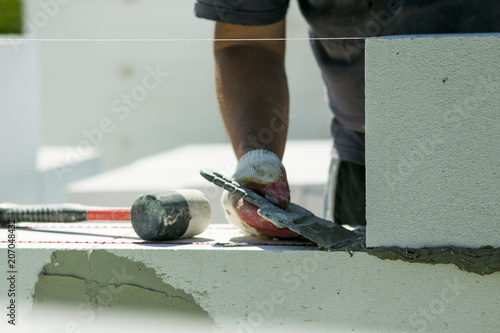 The process of bricklaying. Mason hands installing aerated concrete wall using special glue and tools necessary for brick works. Fresh mortar on aerocrete blocks. Brickwall layer with cement or glue. photo