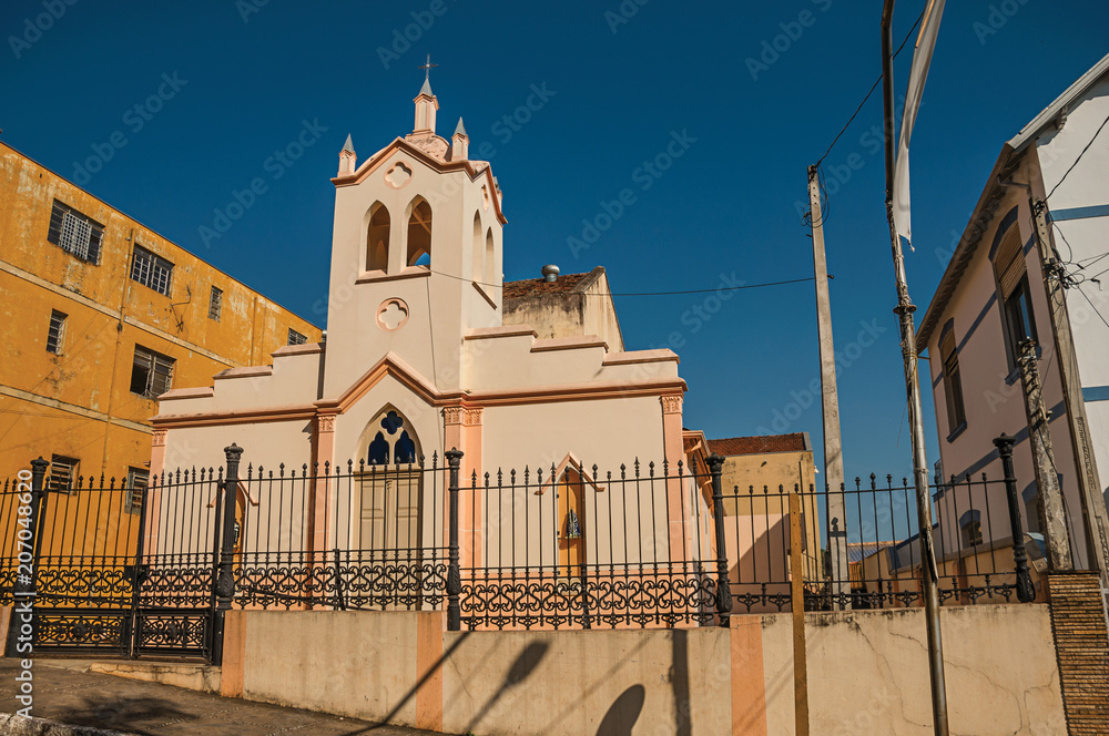 Facade of small church and belfry behind iron fence, in a sunny day at São Manuel. A cute little town in the countryside of São Paulo State. Southeast Brazil.