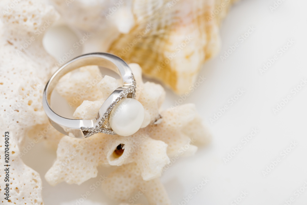 Silver ring with pearl and diamonds on coral against white background Silver ring with pearl and diamonds on coral against white background