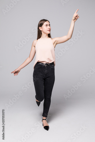 Full length portrait of a smiling girl pointing finger away isolated on a white background