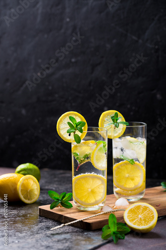 Lemon fruit lime slices caipirinha from Brazil, lemonade mint ice cubes in cold glasses on dark background, alcoholic mojito cockail ice tea green mint leaves, brown sugar spoon, copy space photo