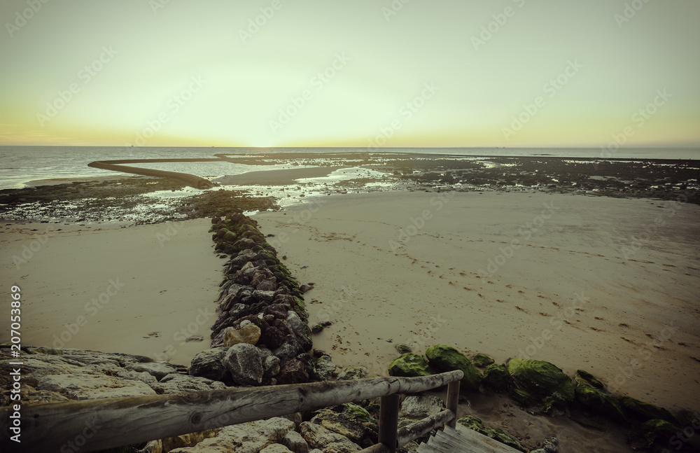 Barandilla de madera que conduce a la playa de Sanlúcar de Barrameda con piedras verdes en la orilla