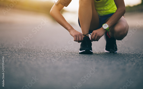 sportswoman tying shoelace before running on city street