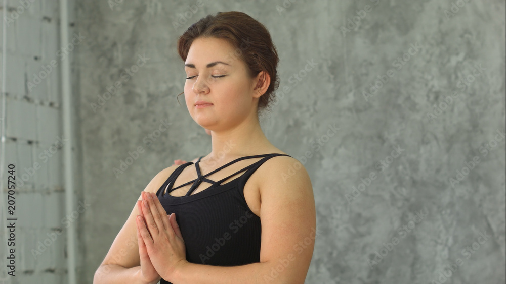 Fototapeta premium Portrait of young beautiful athletic girl practicing indoor yoga with closed eyes and palms in namaste gesture