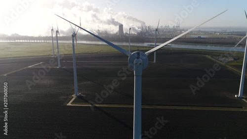 Aerial wind turbine park nuclear power plant and industry in background showing the cooling tower rejecting waste heat to the atmosphere forming thick layers of industrial exhaust 4k high resolution photo