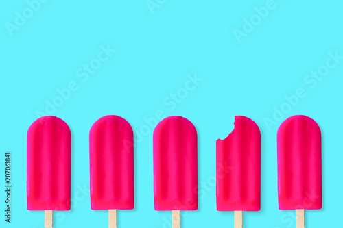 Group of bold pink popsciles on a pastel blue background. One with bite removed. photo