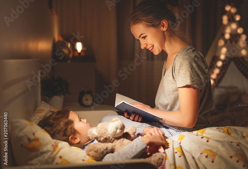 mother and child reading book in bed before going to sleep .