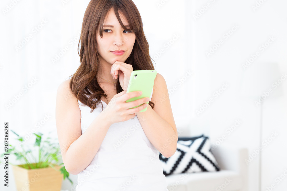 部屋でスマホを見る女性　考える