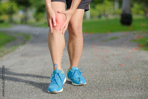 Young fitness woman holding his sports leg injury, muscle painful during training. Asian runner having knee ache and problem after running and exercise outside in summer