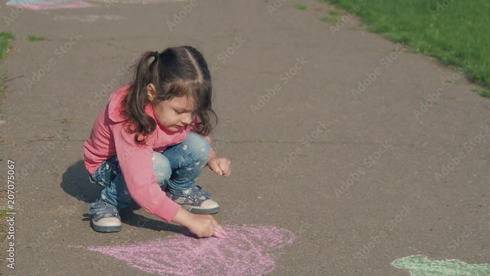 The child paints with chalk. A little girl in the park paints on the asphalt with chalk. The child paints with chalk. A little girl in the park paints on the asphalt with chalk.
