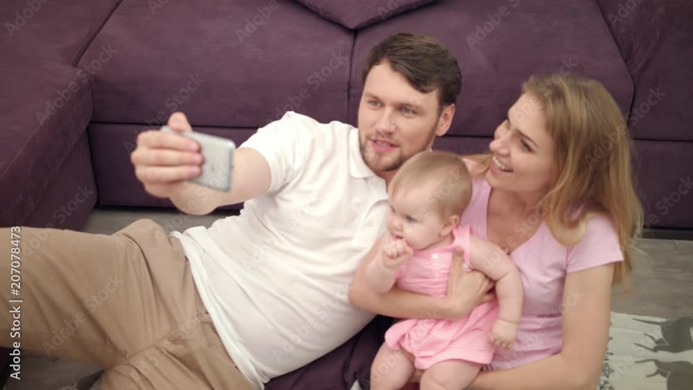 Beautiful family smile for selfie photo. Happy mother and father take selfie picture with little baby. Happiness together. Family selfie photo at home. Portrait of cheerful man and woman with child Beautiful family smile for selfie photo. Happy mother and father take selfie picture with little baby. Happiness together. Family selfie photo at home. Portrait of cheerful man and woman with child
