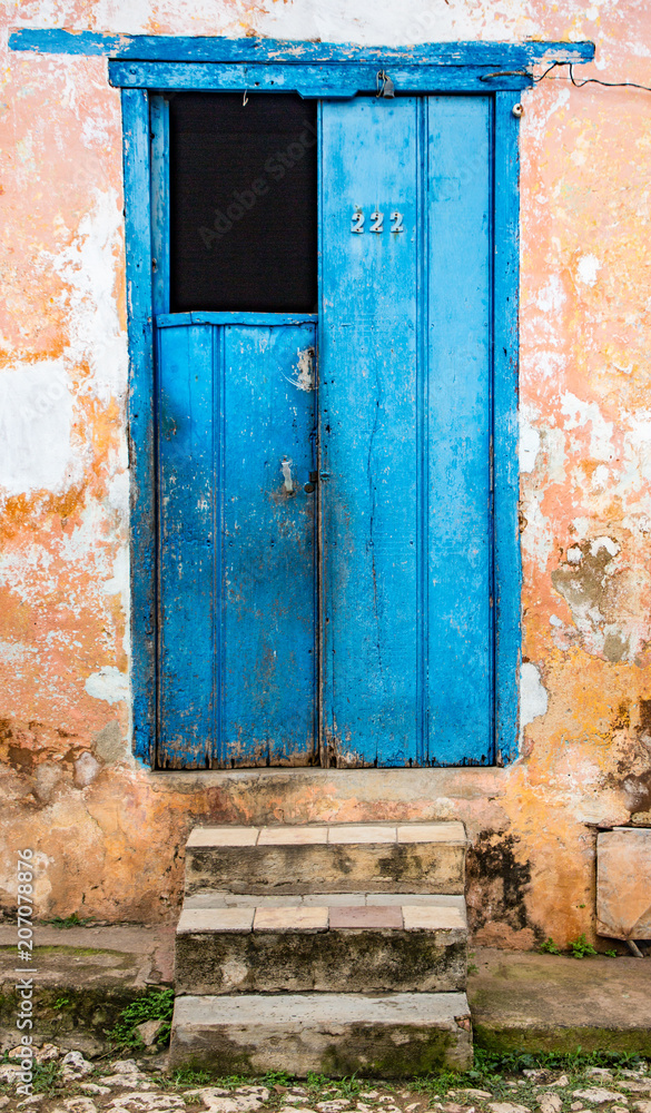 Half-open blue door on tattered yellow wall with stone steps