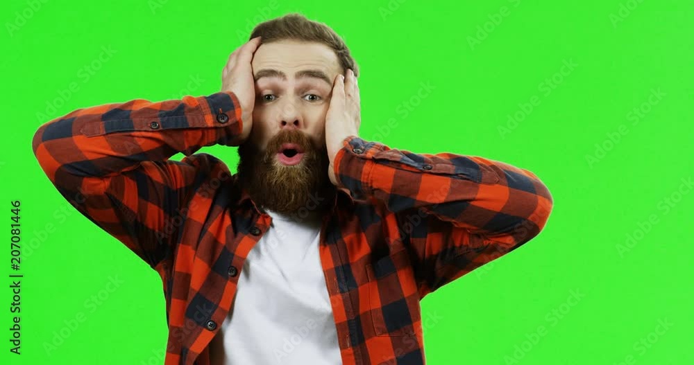 Portrait of the emotional man with a beard holding his head and looking relieved on the green screen background. Chroma key.