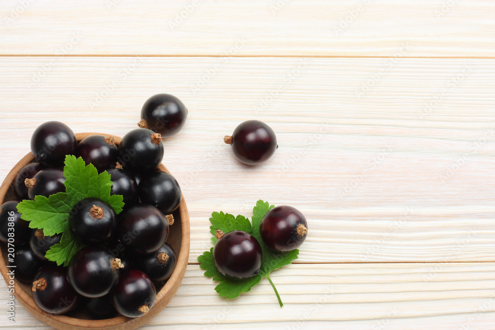 black currant in wooden bowl with green leaf on white wooden background. top view with copy space black currant in wooden bowl with green leaf on white wooden background. top view with copy space
