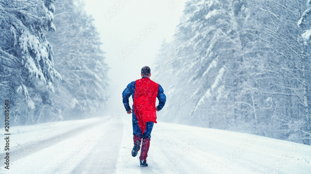 Superman with a red cloak runs on a snowy road in the snow-covered forest Superman with a red cloak runs on a snowy road in the snow-covered forest