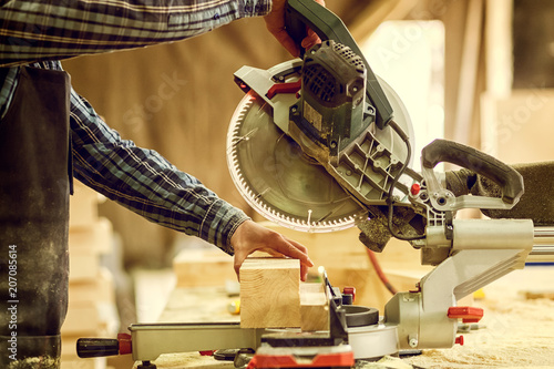 Carpenter in work clothes  doing woodwork in carpentry. small buiness owner cut on wood plank  with circular saw in workshop