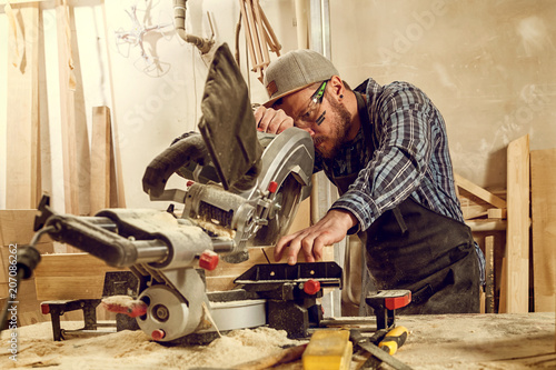 experienced carpenter using circular saw for cutting wooden boards. Construction details of male worker or handy man with power tools