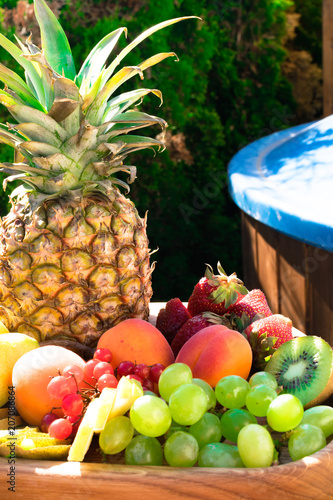 Mix of different exotic fresh colorful fruits on dark wooden table and green trees photo