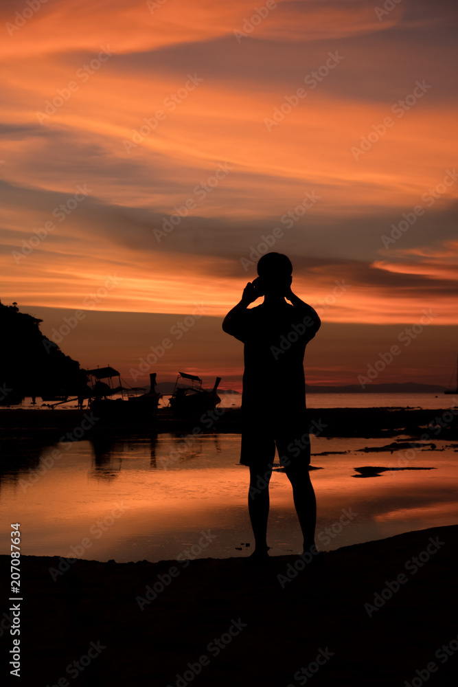 Fototapeta premium Silhouette of Man taking a sunset with a smartphone at Loh Dalum Bay, Phi Phi Island, Krabi, Thailand.
