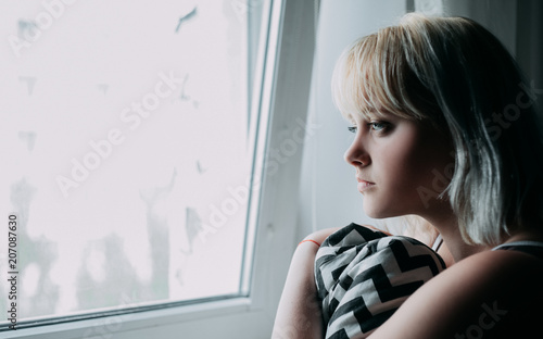 Portrait of depressed young blond woman near window at home. Sadness, nostlagic, depression. Free Download Portrait of depressed young blond woman near window at home. Sadness, nostlagic, depression. - GFXLoad