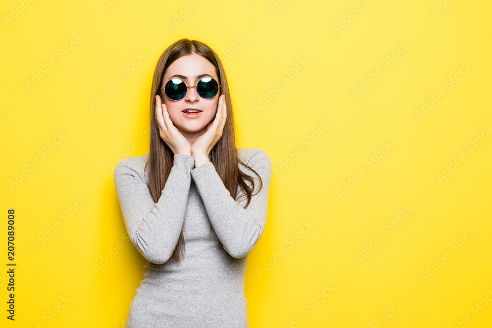 Young fashion girl with sunglasses in dress hands on ching on yellow background Young fashion girl with sunglasses in dress hands on ching on yellow background