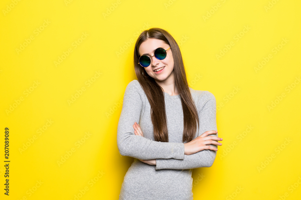 Young fashion girl with sunglasses in dress with crossed hands on yellow background Young fashion girl with sunglasses in dress with crossed hands on yellow background