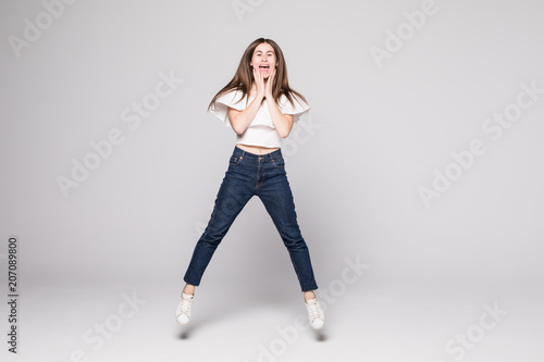 Full length portrait of a cheerful happy woman jumping and looking away isolated over white background