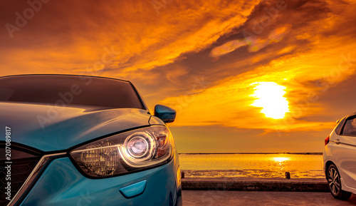Blue and white compact SUV car with sport and modern design parked on concrete road by the sea at sunset. Environmentally friendly technology. Business success concept. Car with open headlamp light. © Artinun