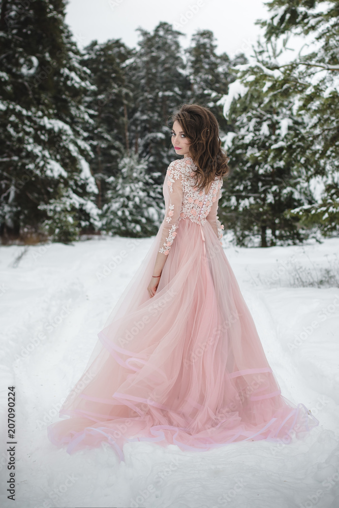 Girl in a beautiful pink dress in a winter forest