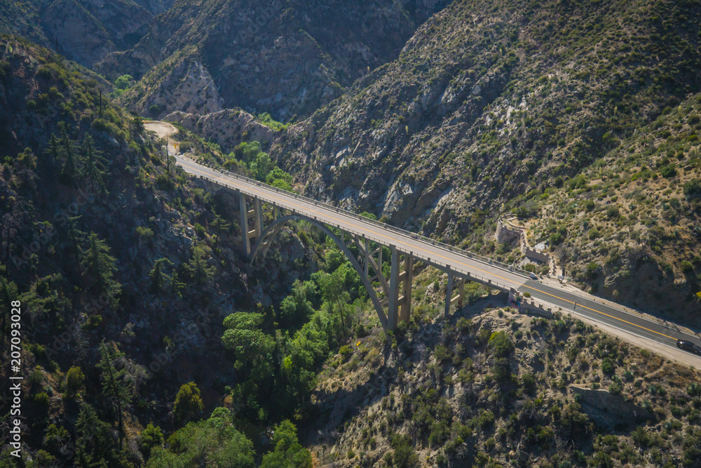 Fototapeta premium Long arch bridge stretches above a wooded canyon in the mountains of southern California.