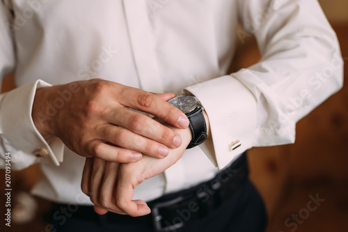 The groom in a white shirt and trousers looks at the wristwatch