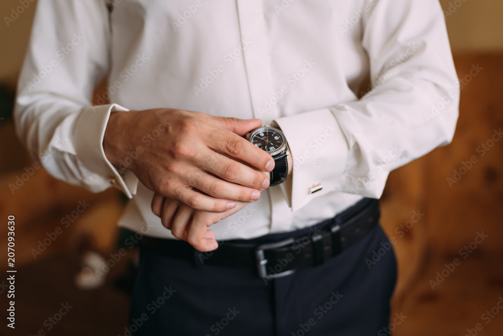 The groom in stylish clothes looks at the wristwatch.