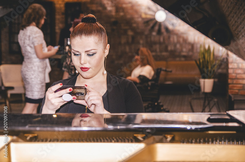 Young lady sitting on the piano and checking her mobile phone.