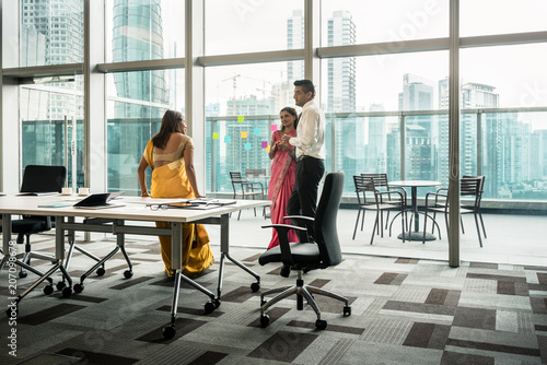 Three Indian employees talking during break in the meeting room of a modern business building