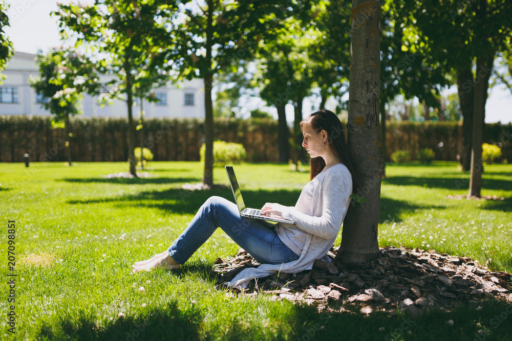 Young successful businesswoman in casual clothes. Woman sit on grass ground, working on laptop pc computer in city park on green lawn outdoors on nature. Mobile Office. Freelance business concept. Young successful businesswoman in casual clothes. Woman sit on grass ground, working on laptop pc computer in city park on green lawn outdoors on nature. Mobile Office. Freelance business concept.