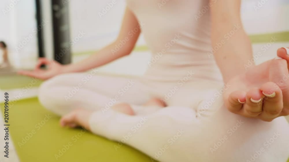 Young woman in beige jumpsuit sitting on green mat and practicing yoga at light studio class room. Meditating in lotus pose with Jnana Gian mudra. Om. Dolly shot. Young woman in beige jumpsuit sitting on green mat and practicing yoga at light studio class room. Meditating in lotus pose with Jnana Gian mudra. Om. Dolly shot.