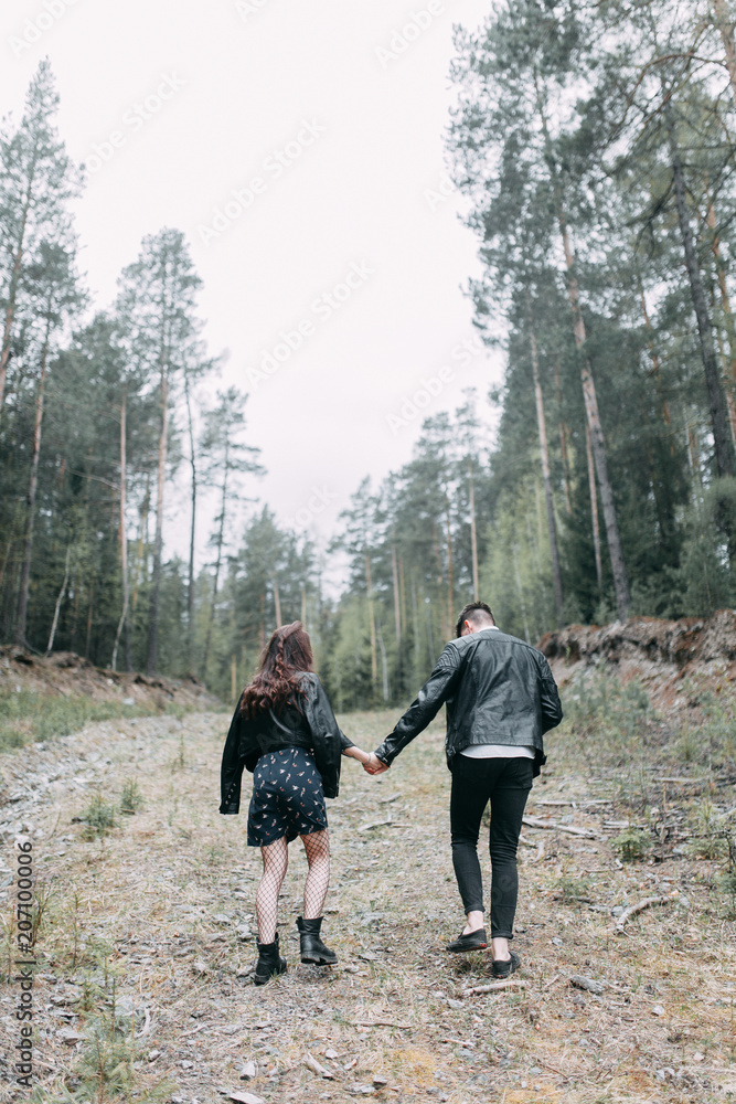 Young stylish couple in the forest, running around the Park and laughing. Modern people on a walk. Beautiful girl with tattoos. Loving young man and girl. mountain Park with pine forest Young stylish couple in the forest, running around the Park and laughing. Modern people on a walk. Beautiful girl with tattoos. Loving young man and girl. mountain Park with pine forest
