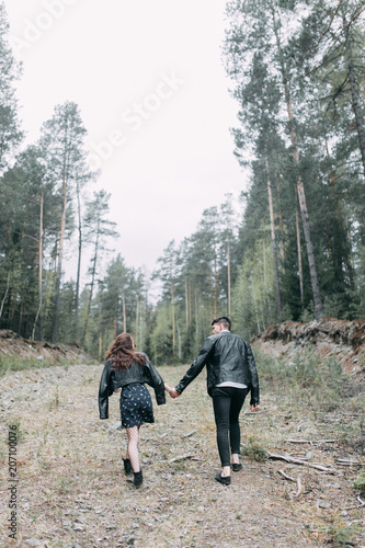 Young stylish couple in the forest, running around the Park and laughing. Modern people on a walk. Beautiful girl with tattoos. Loving young man and girl. mountain Park with pine forest