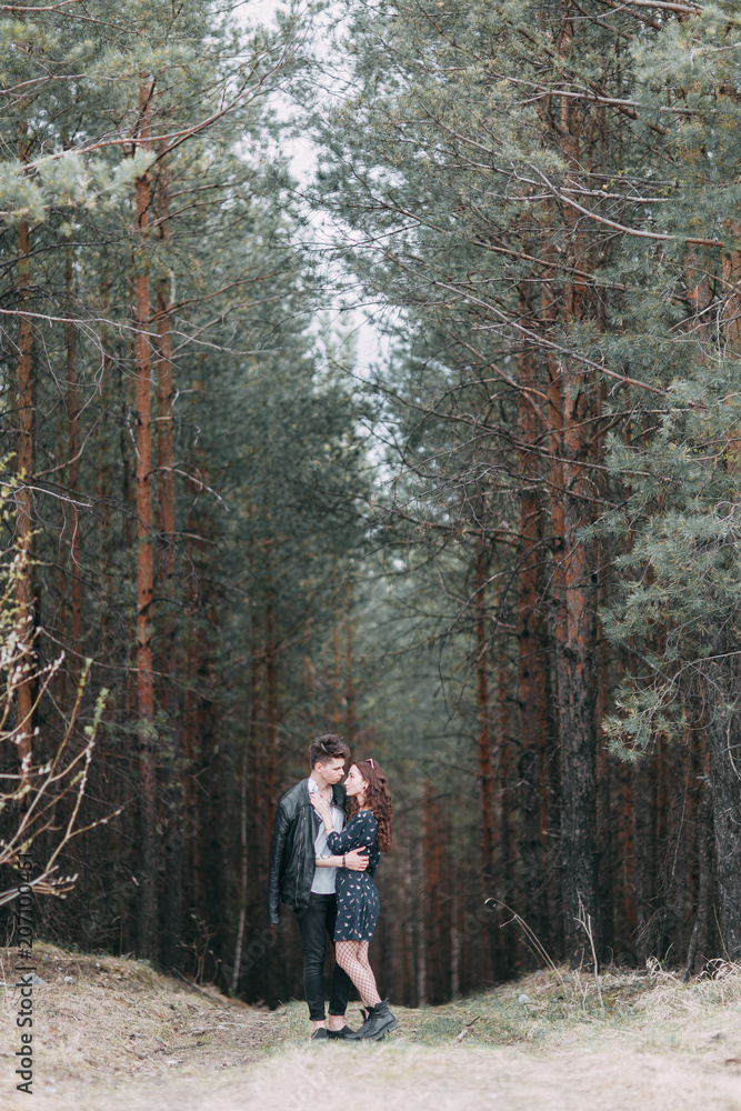 Obraz premium Young stylish couple in the forest, running around the Park and laughing. Modern people on a walk. Beautiful girl with tattoos. Loving young man and girl. mountain Park with pine forest