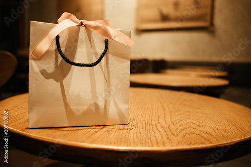 celebration background paper bag with ribbon place on wood table in restaurant with copy space. image for present, birthday, christmas, object, decoration, nobody concept