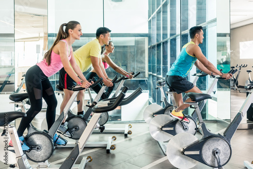Fototapeta Naklejka Na Ścianę i Meble -  Rear low-angle view of two fit women with an active lifestyle burning calories during indoor cycling class in a modern fitness club