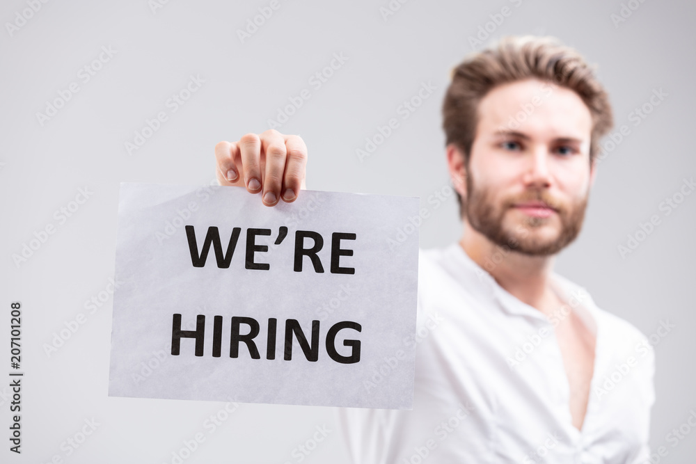 Bearded man holding up a We're Hiring sign Bearded man holding up a We're Hiring sign